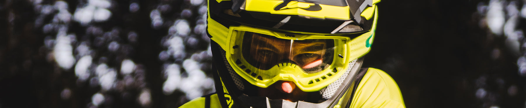 Nahaufnahme einer Person mit einem leuchtend gelben Motocross-Helm und einer Schutzbrille und konzentriertem Gesichtsausdruck. Der dunkle, unscharfe Hintergrund verstärkt den konzentrierten Blick des Fahrers.