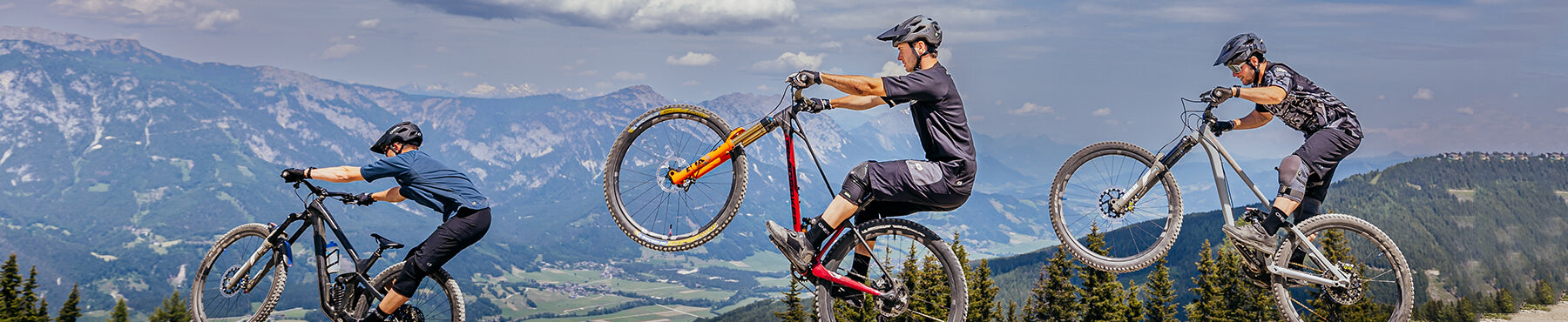 Drei Mountainbiker führen Stunts in der Luft vor einer Kulisse aus Bergen und Tälern vor. Sie tragen Helme und Ausrüstung und zeigen ihr Können in einer Outdoor-Abenteuerumgebung.