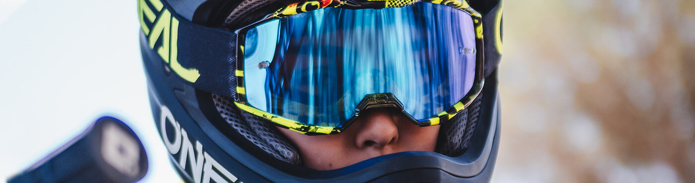 Nahaufnahme einer Person, die einen Helm mit verspiegelter Schutzbrille trägt. Das blau-gelbe Design spiegelt die Landschaft im Freien wider. Der Hintergrund ist verschwommen und lenkt die Aufmerksamkeit auf den Helm und die Schutzbrille.