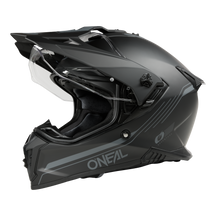 Der O'NEAL A-SRS Helmet SOLID ist ein mattschwarzer Motorradhelm mit transparentem Visier und elegantem Offroad-Design mit aerodynamischen Linien und zusätzlichen Belüftungsöffnungen. Das kultige O'Neal-Logo ziert die Seite vor einem schwarzen Hintergrund.