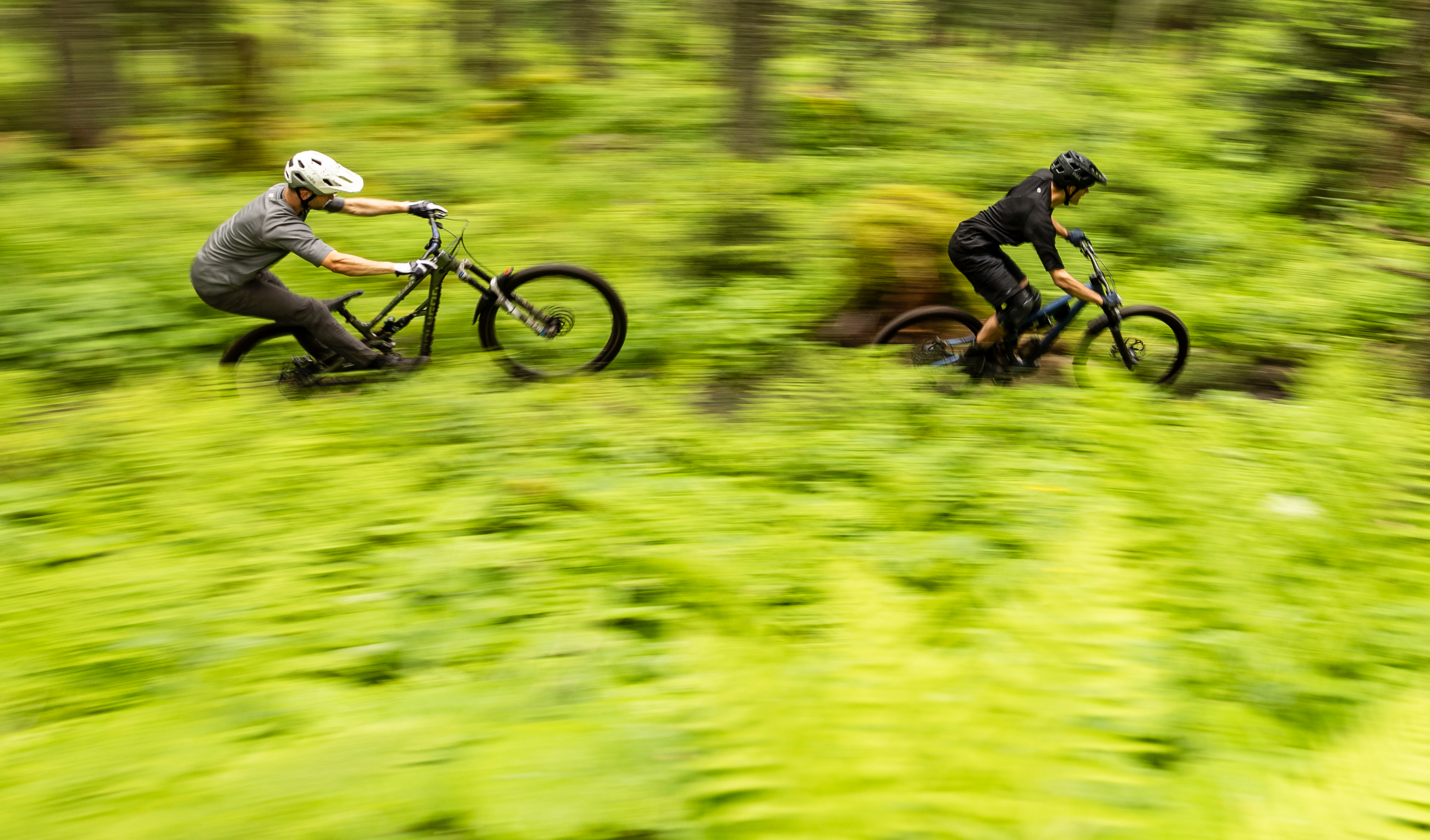 Zwei Mountainbiker fahren schnell auf einem Trail durch einen grünen Wald